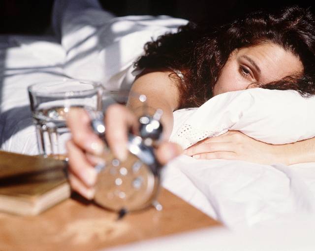 Woman lying in bed, turning off alarm clock