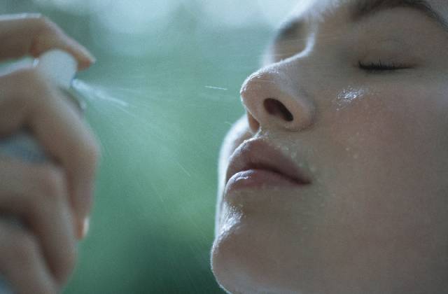 Woman spraying water on face with eyes closed