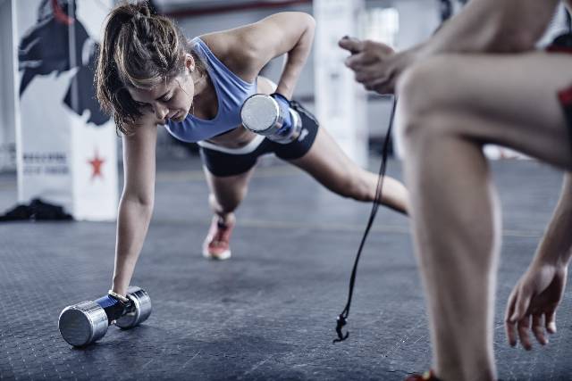 Fitness trainer keeping time with woman doing dumbell push-ups