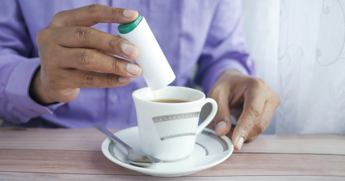 Egy ember édesítőt szór a kávéjába