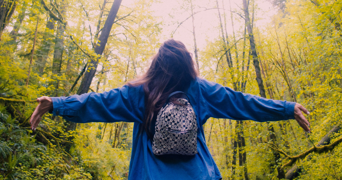 Nő az őszi erdőben boldogan széttárja a karját.