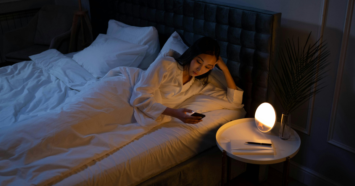 Nő fekszik éjjel az ágyban ébren, mellette éjjeli lámpa világít.