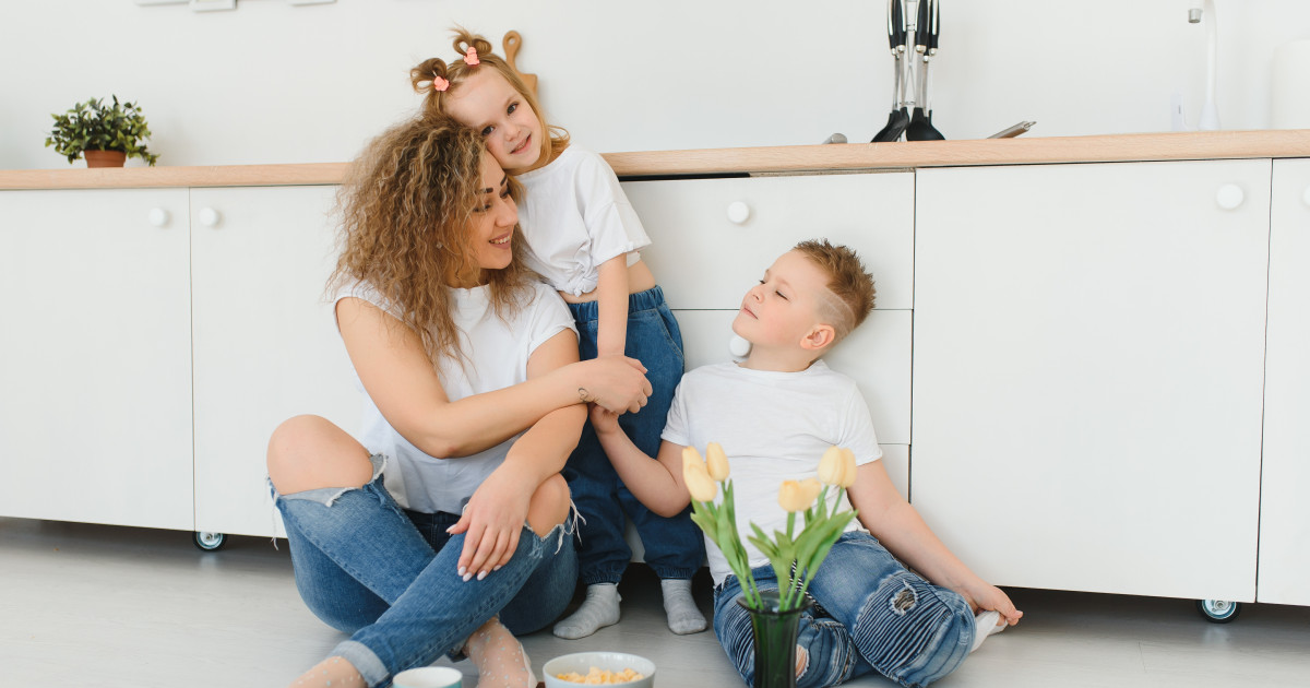 Fiatal anya a konyhában ül kislányával és kisfiával.