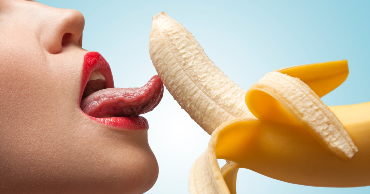 Vörös rúzsos nő megnyal egy banánt a nyelvével.