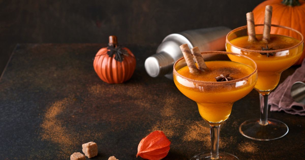Két pohár pumpkin spice margarita koktél, díszítésként fahéjrudakkal, a háttérben koktél 