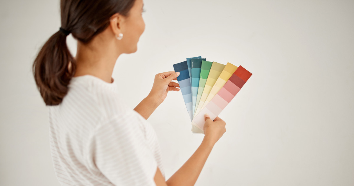 Nő áll a fehér fa előtt, festés előtt színpalettával a kezében.